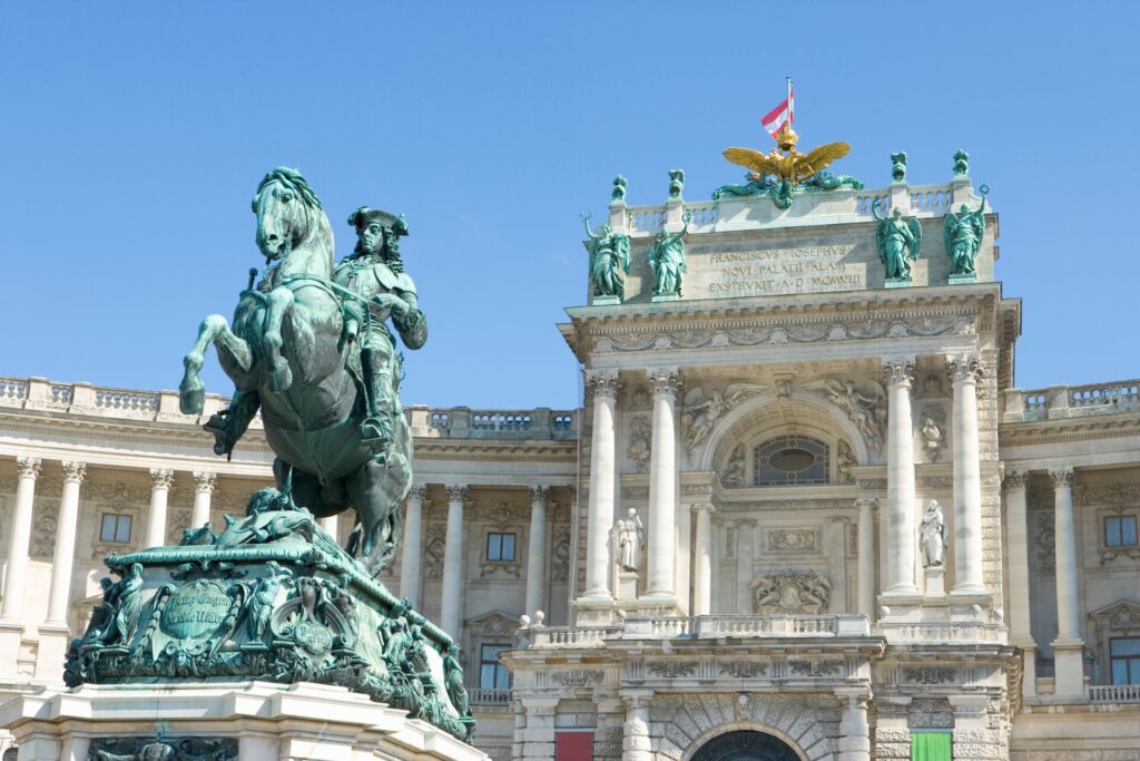 A green horse statue rears in front of the white a green ornate facade of Vienna's Hofburg Palace. 