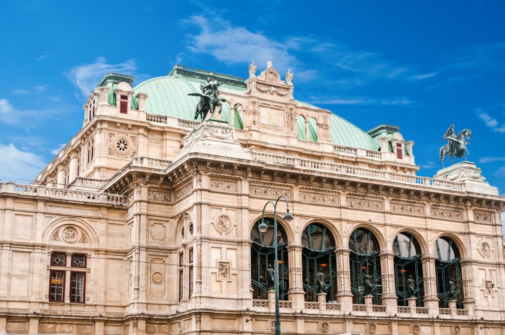 The Vienna State Opera House with a pale green roof, statues of flying horses and five large arched windows.