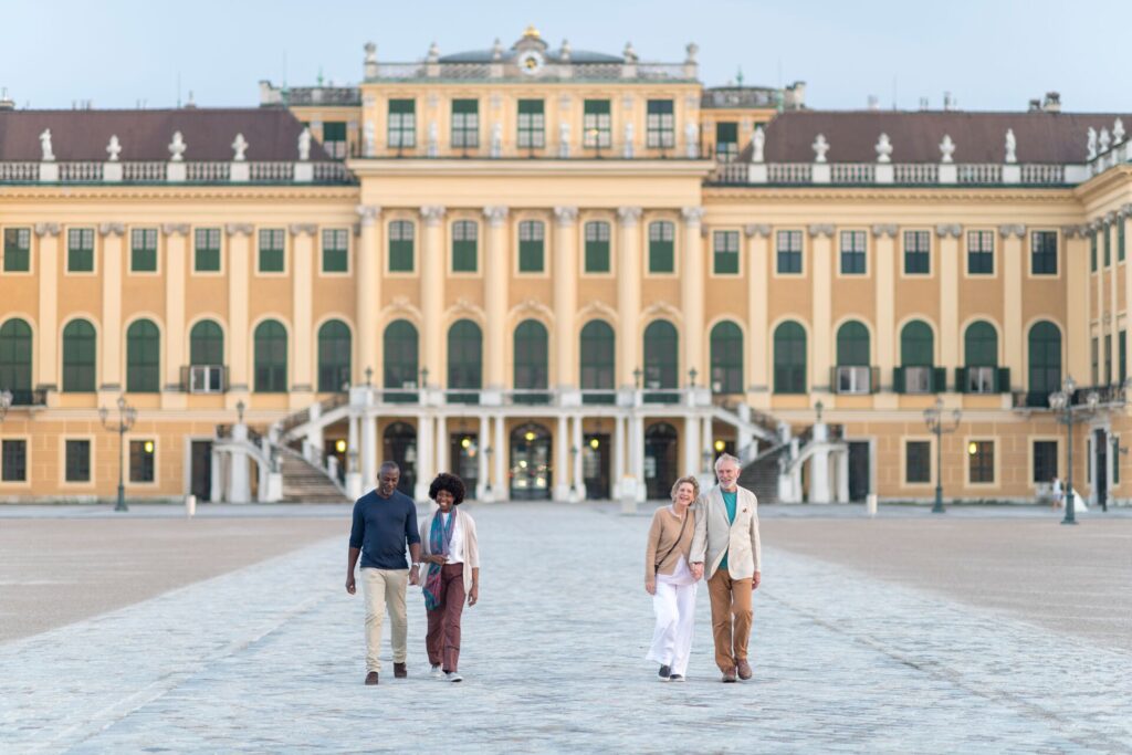 Two couples walk in front of Vienna's Schönbrunn Palace, with its yellow and green grand facade.