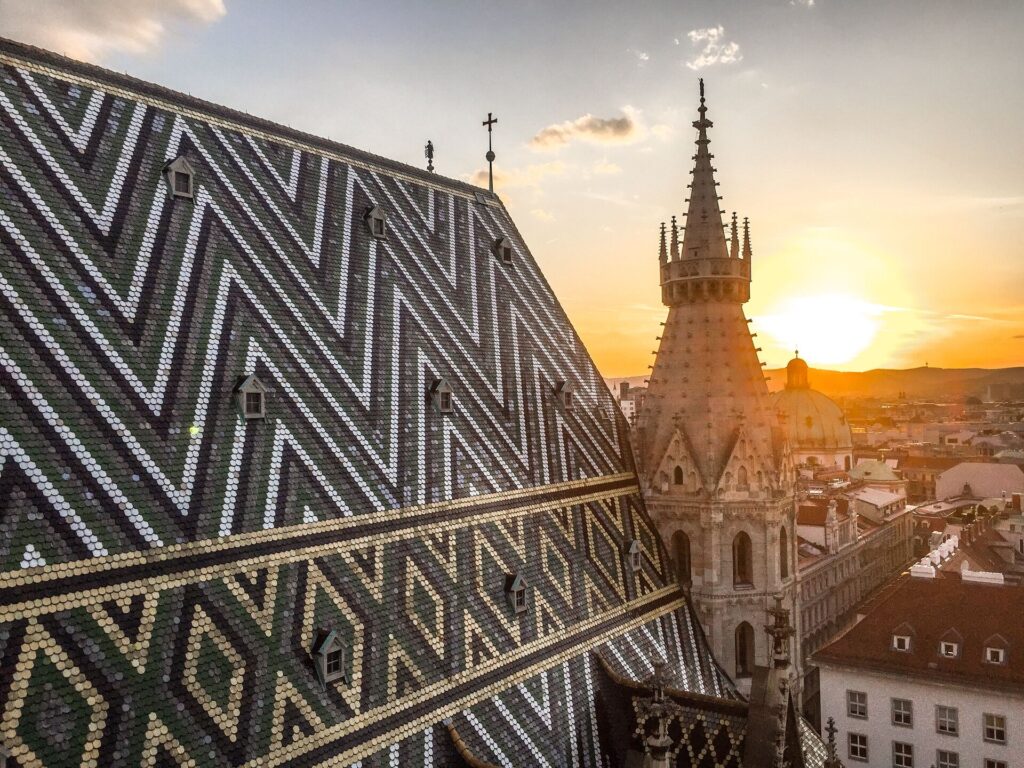 New at sunset over black and white zig zag tiled roof and ornate turret of St Stephen's Cathedral in Vienna.