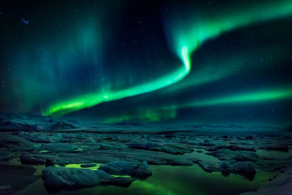 bright green streaks cross the night sky in Iceland, with a rocky landscape below glowing in the Northern Lights