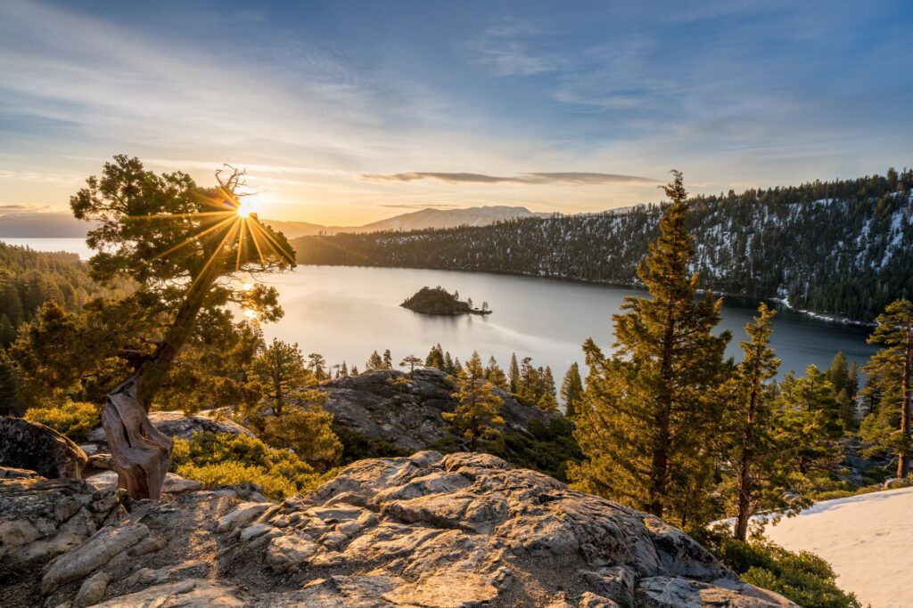 the sun sets over Norris Spring, California, with a lake flanked by evergreen trees, and rocks in the foreground