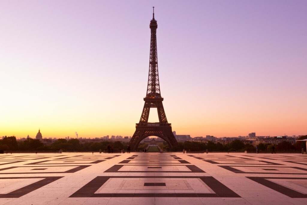 The iron coloured Eiffel Tower in Paris against a sunset sky of yellow and purple, with a large plate in front.