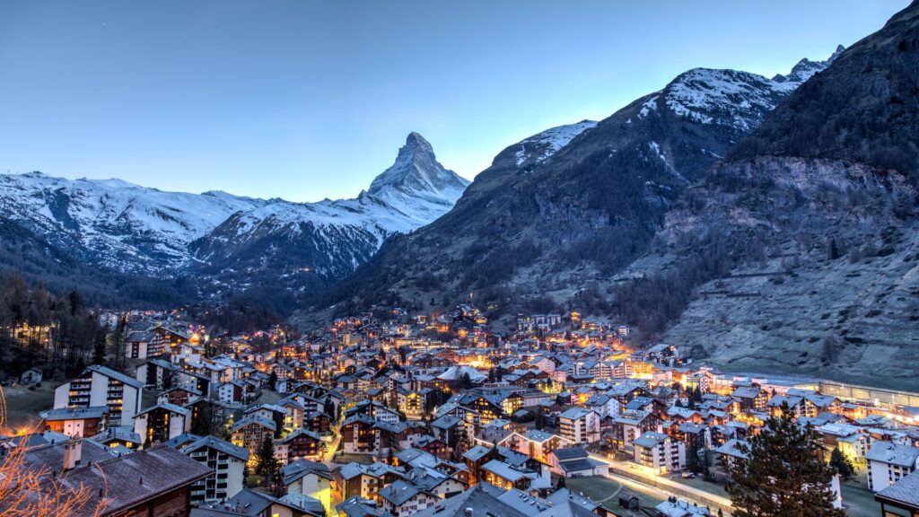 Houses in the ski resort town of St Moritz in Switzerland glow amongst the Alps, everything covered in snow.