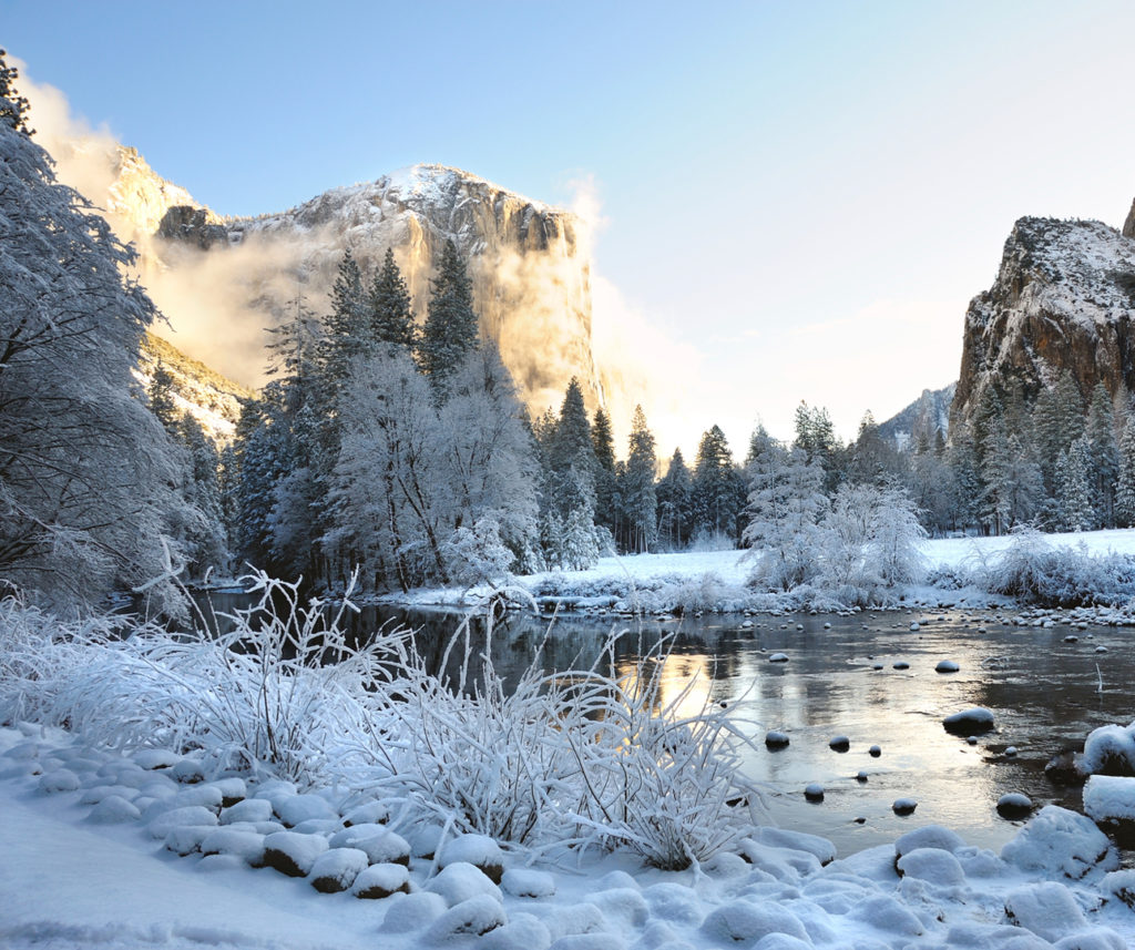 A snow covered landscape with a lake and mountains and sunny bright blue sky.