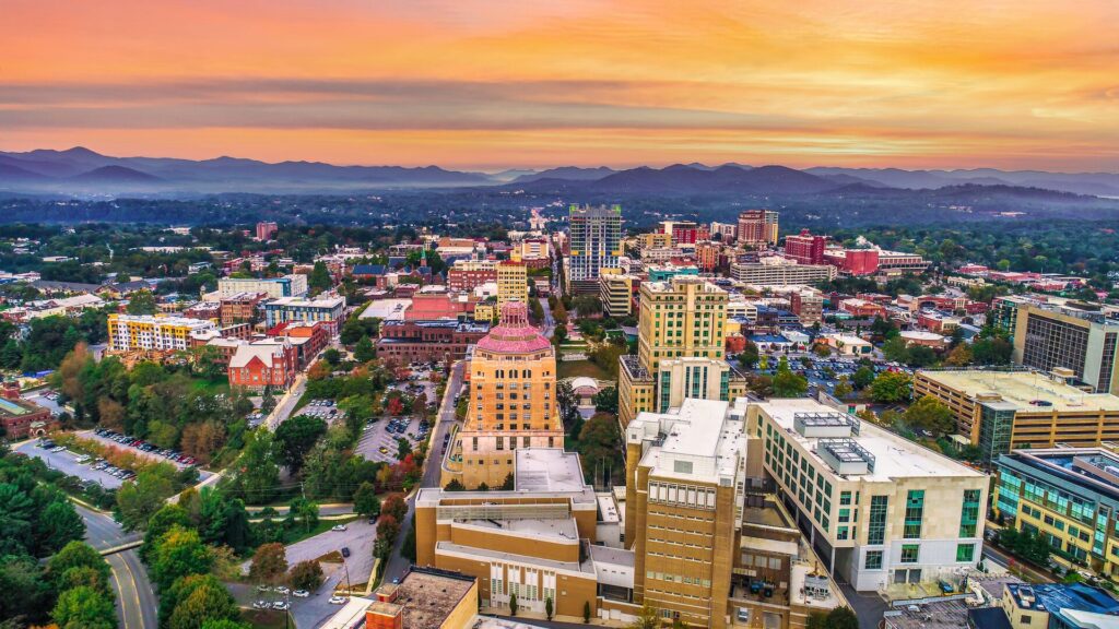 Aerial shot of the buildings and parks of Asheville, USA, with a dramatic sunset sky.