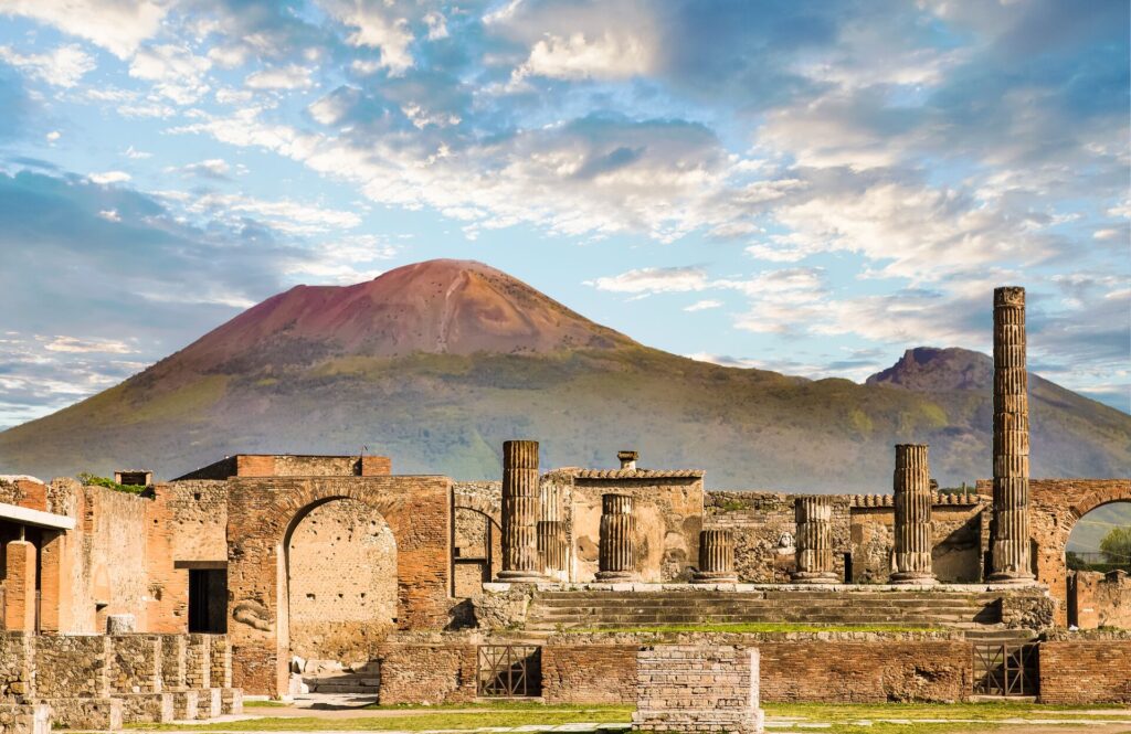 The running of the ancient Italian city of Pompeii with Mount Vesuvius in the background and a blue cloudy sky.