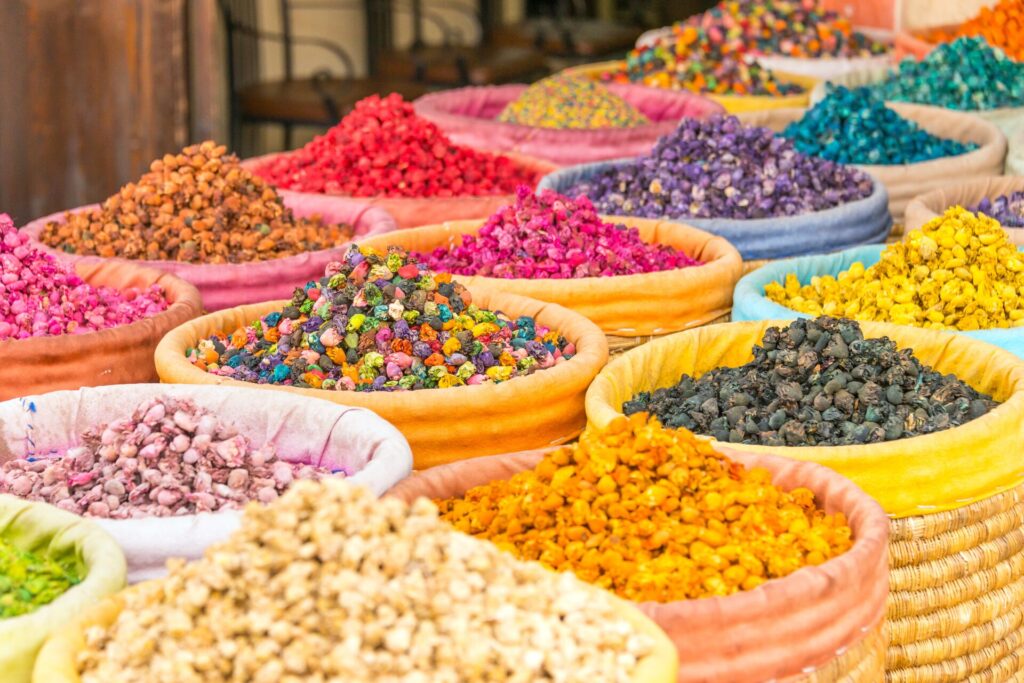 Rows of bright coloured spices in woven pots in yellow, pink, black, read, purple and green.