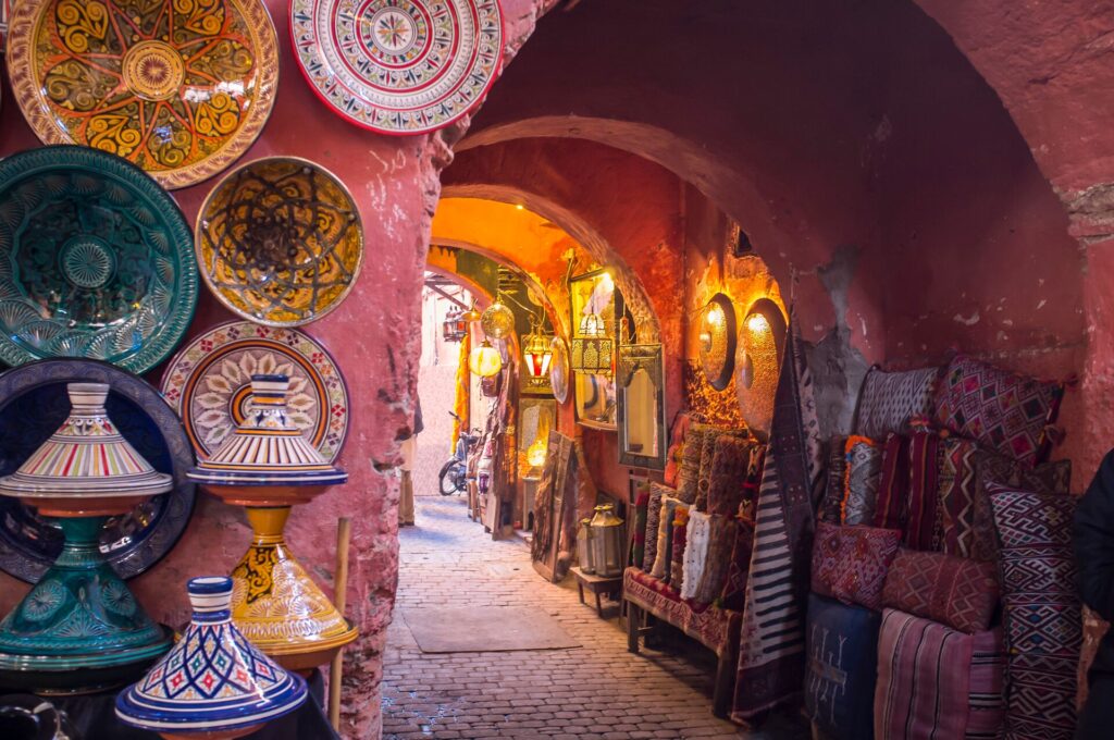 Colorful ceramics, traditional rugs and copperware on show in pink painted low alleyways of a bazaar in Morocco.