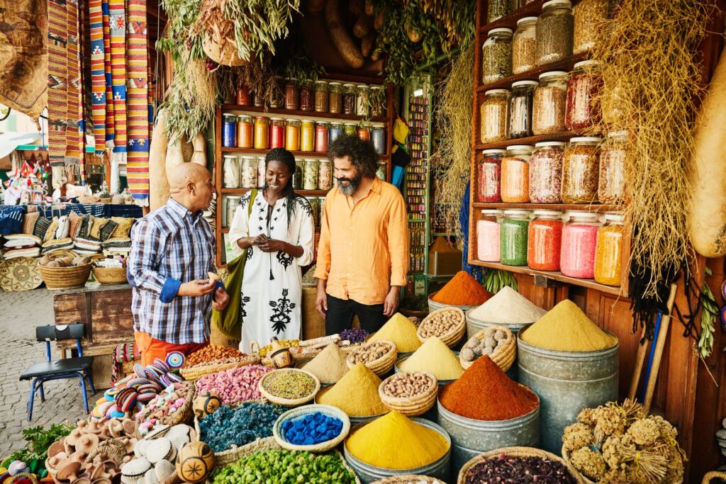 Two tourists talk with a local vender selling colourful spices at a bazaar in Morocco