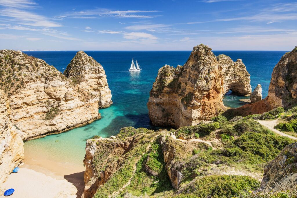 Cliffs at the Slgarve in Portugal with green waters, golden beaches and a bright blue sky.