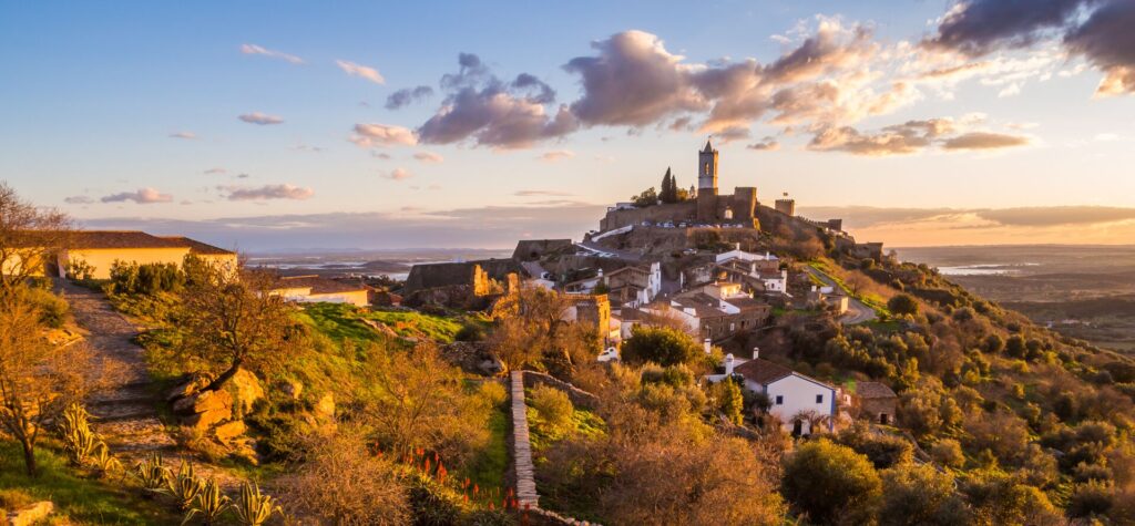 An old town set atop a hill in Portugal, with fields and trees all around.