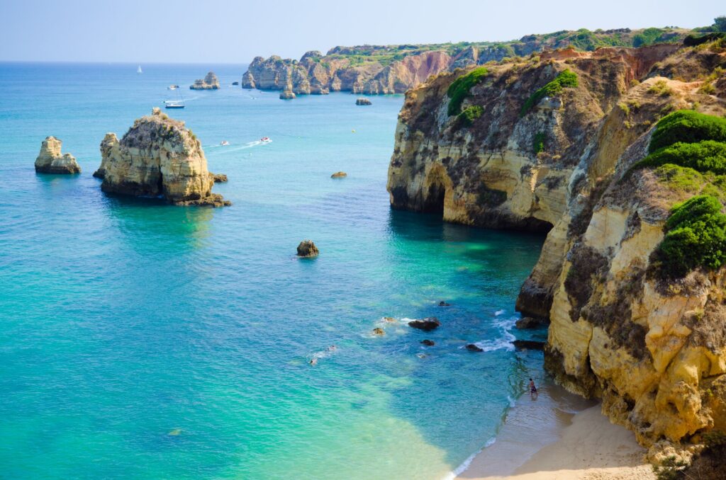 Tall sea cliffs of the Algarve in Portugal with a turquoise sea and a golden beach.