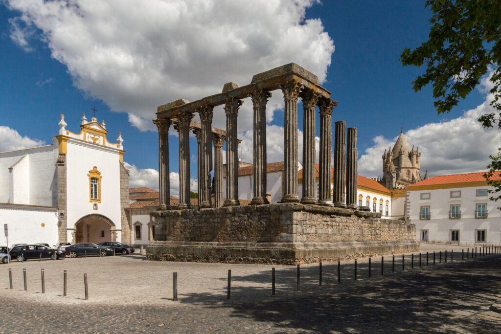 Dark stone columns of the Roman temple of Diana in Evora, Portugal , with white houses and red roofs surrounding it.