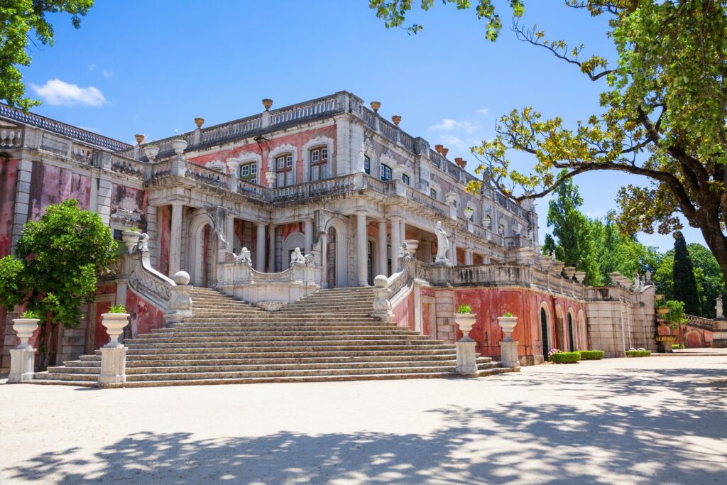 A Palace iN Portugal with a red facade and white steps, with green trees in the foreground.