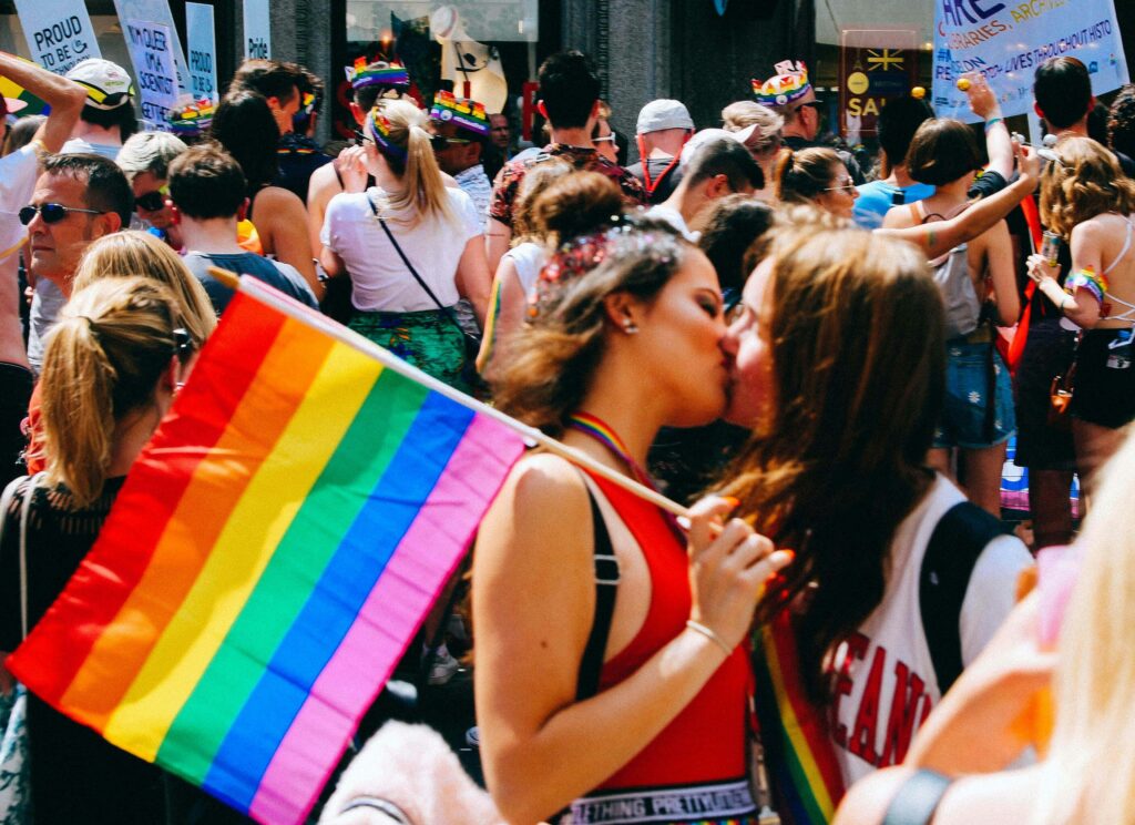 A couple embrace whilst holding a rainbow flag, amongst crowd of people celebrating Pride in London, UK.