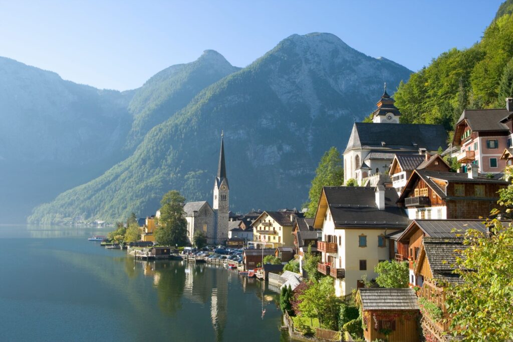 White houses and a church lit alongside a large blue lake with green mountains in the background.