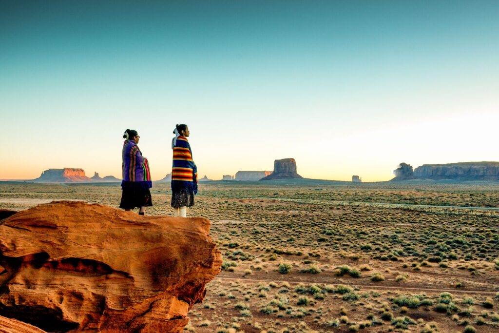 Two Native American women looking out over the desert from atop a rocky outcrop