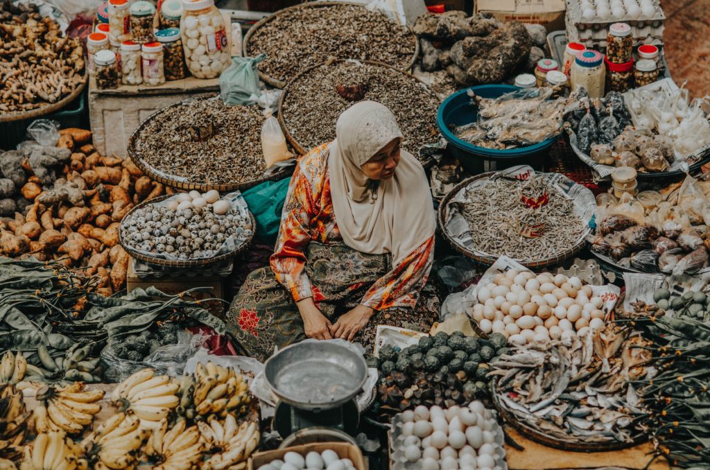 A woman sits surrounded by vegetables and produce in a market.