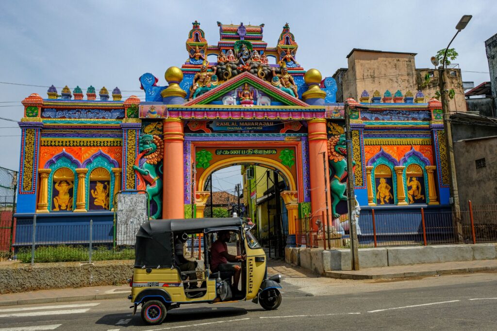 A brightly painted entrance gate of blue, green, pink and purple with a traditional tun tun in front in Sri Lanka.