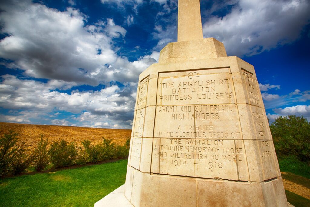 A cream stone memorial stands on a green field, with golden crops and a blue and white sky, remembering those who lost their lives in the Battle of the Somme.