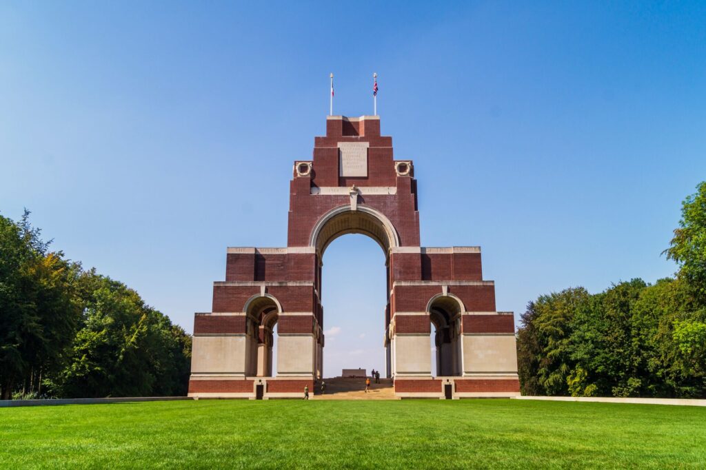 A large memorial arch in dark red brick stands on the bright green Somme Battlefields and a memorial.