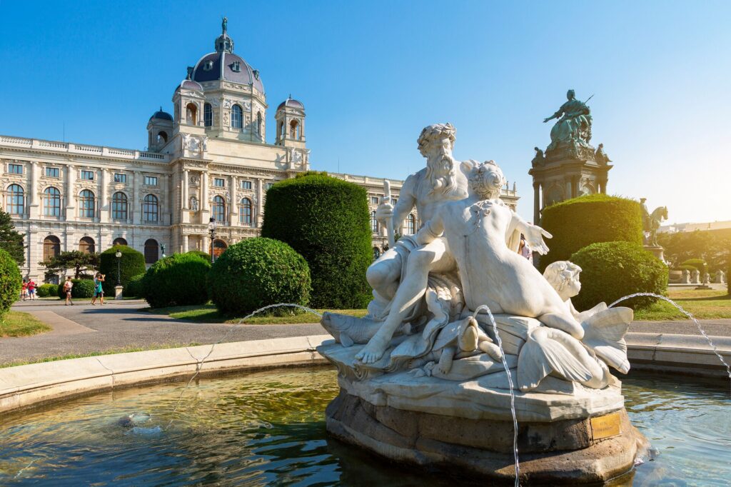 A white star of a man and woman sits in the middle of an ornate pond, in front of an opulent palace in Vienna, Austria.