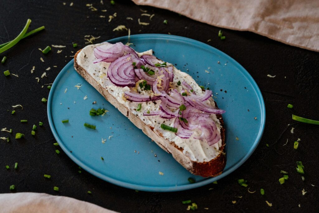 A plated Smørrebrød with cream cheese and onion topping.