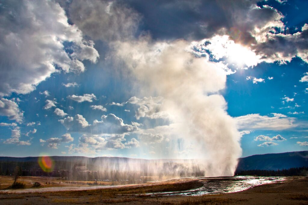 Old Faithful in Yellowstone National Park erupts, with white steam blowing up into the bright blue sky