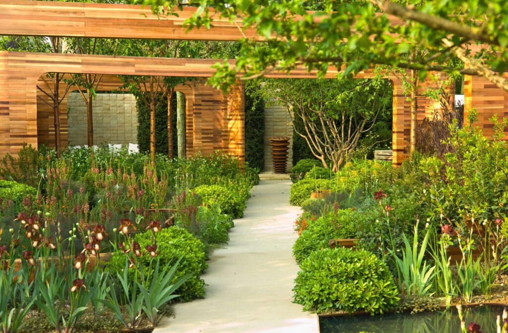 A wooden pavilion with rows of manicured green shrubs and blooms in front at the Chelsea Flower Show