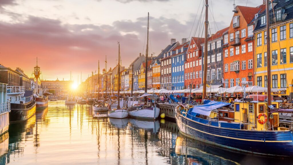 The European city of Copenhagen, Denmark Clinton in the fall sun, with red, yellow and blue houses, a river and colorful boats moored not he sides.