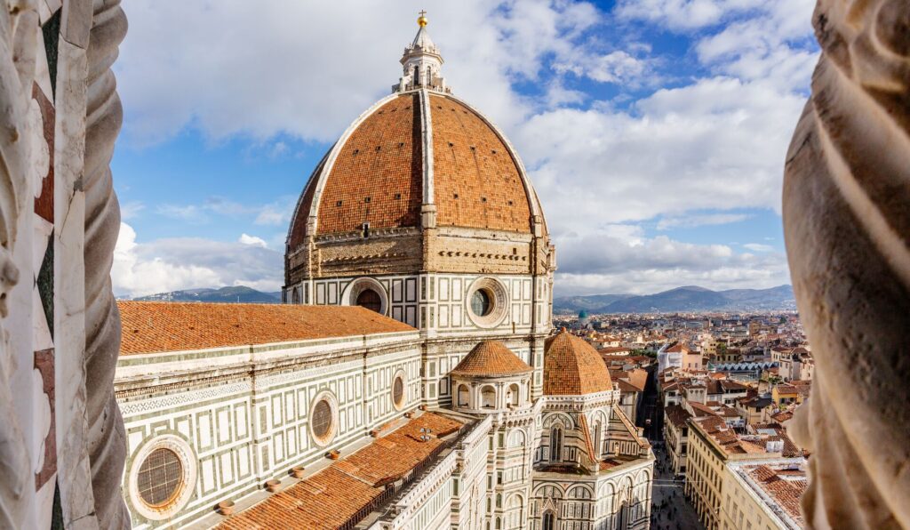 A high view out over the ornate red and white palaces of Florence, Italy, with a bright sky.