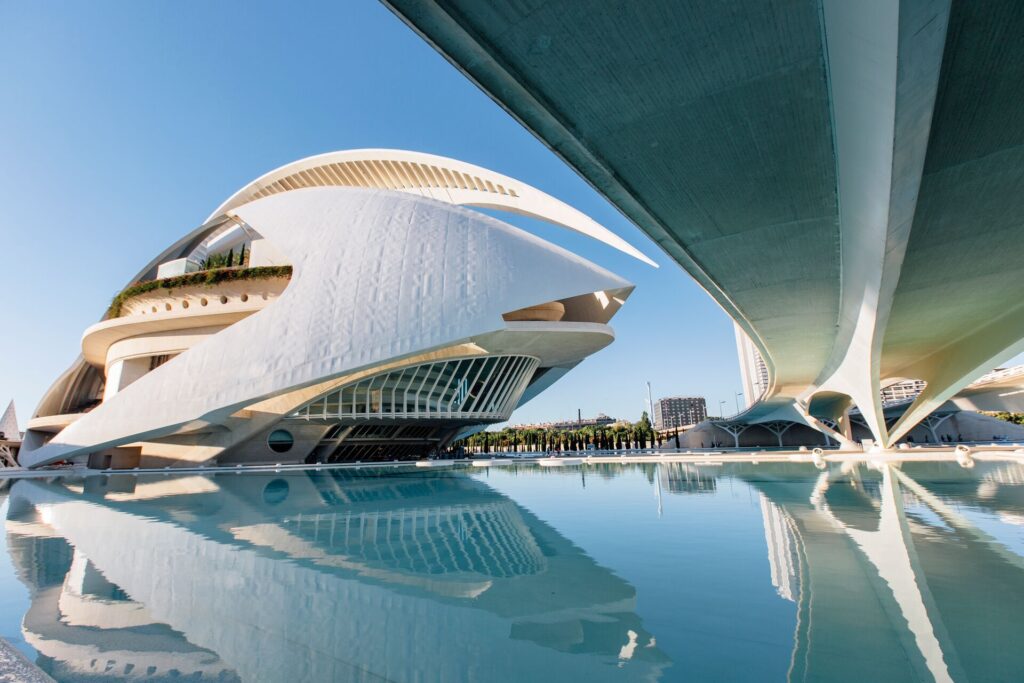 Modern, white a silver buildings of The City of Arts and Science, Valencia, reflecting in the clear, blue water below.