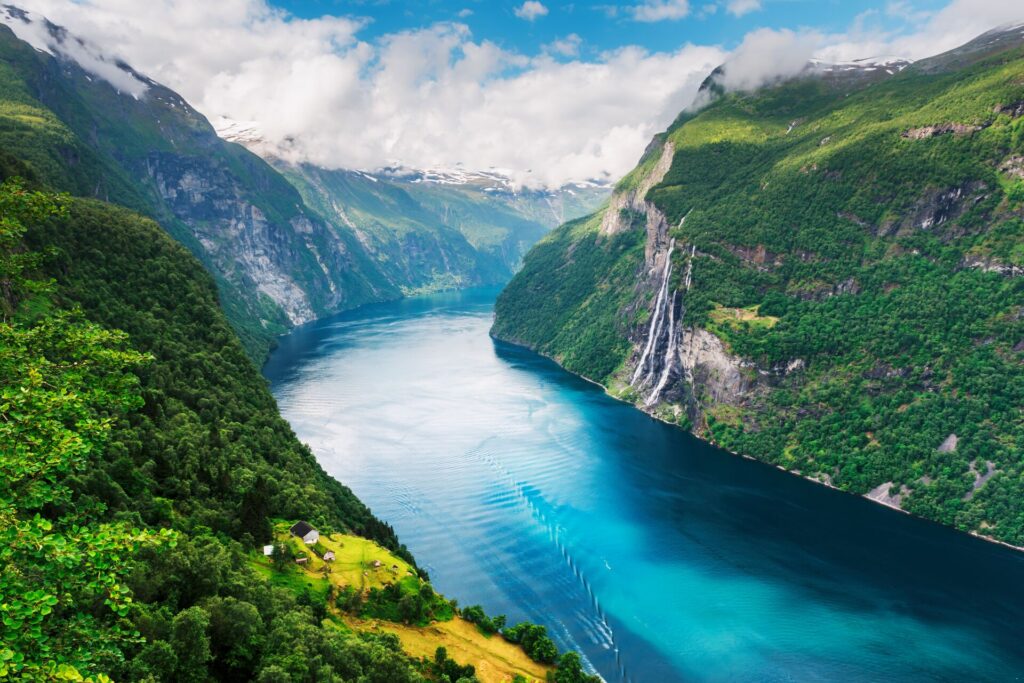 A huge river curves around a valley, bright blue and rippling. The valley cliffs are rife with lush vegetation. It's one of Scandinavia's beautiful fjords