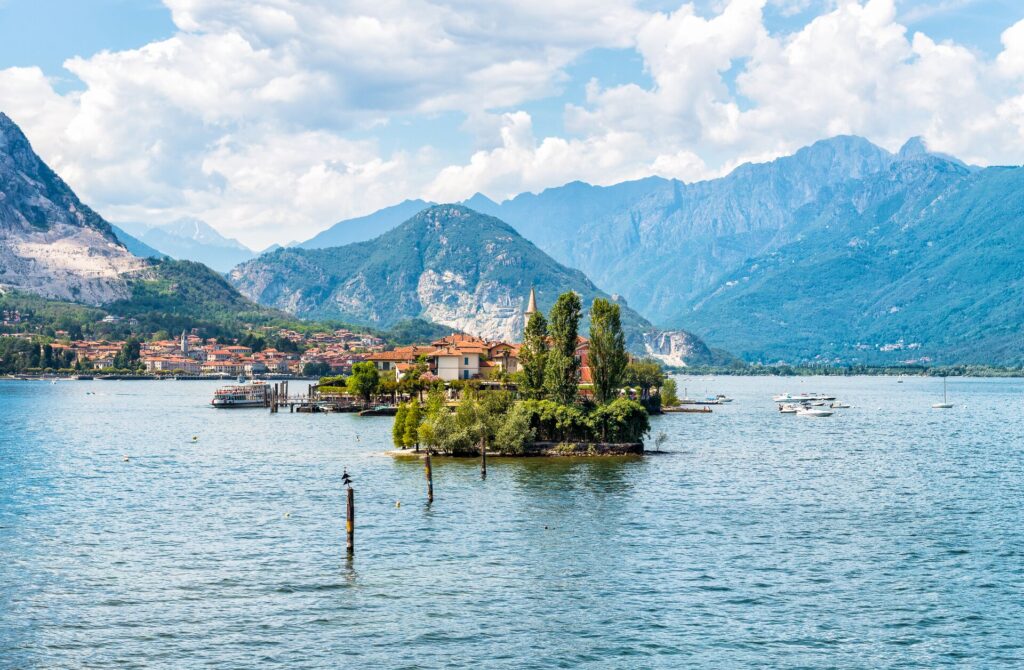A wide shot of a house on Lake Maggiore in Italy, with blue water and mountains in the background