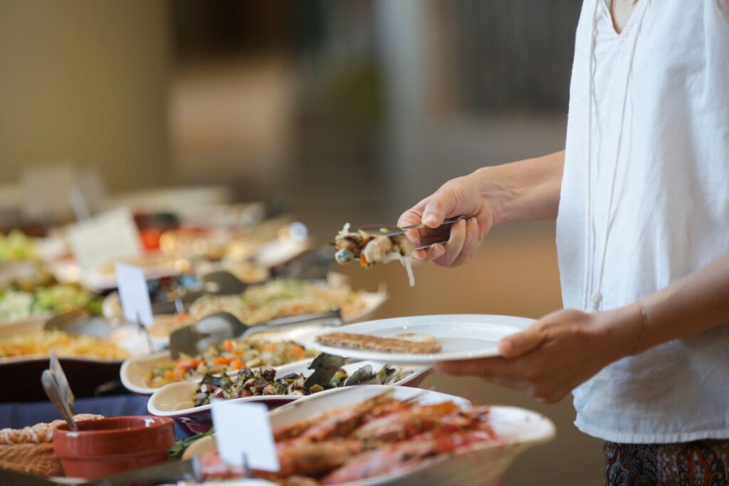 A woman fills a plate from a buffet of various dishes.