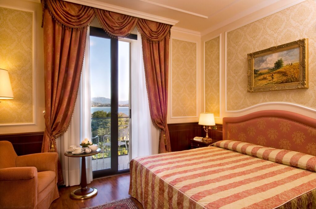 An elegant room of the Lake Maggiore hotel Simplon with natural shades and a view of the lake and mountains.