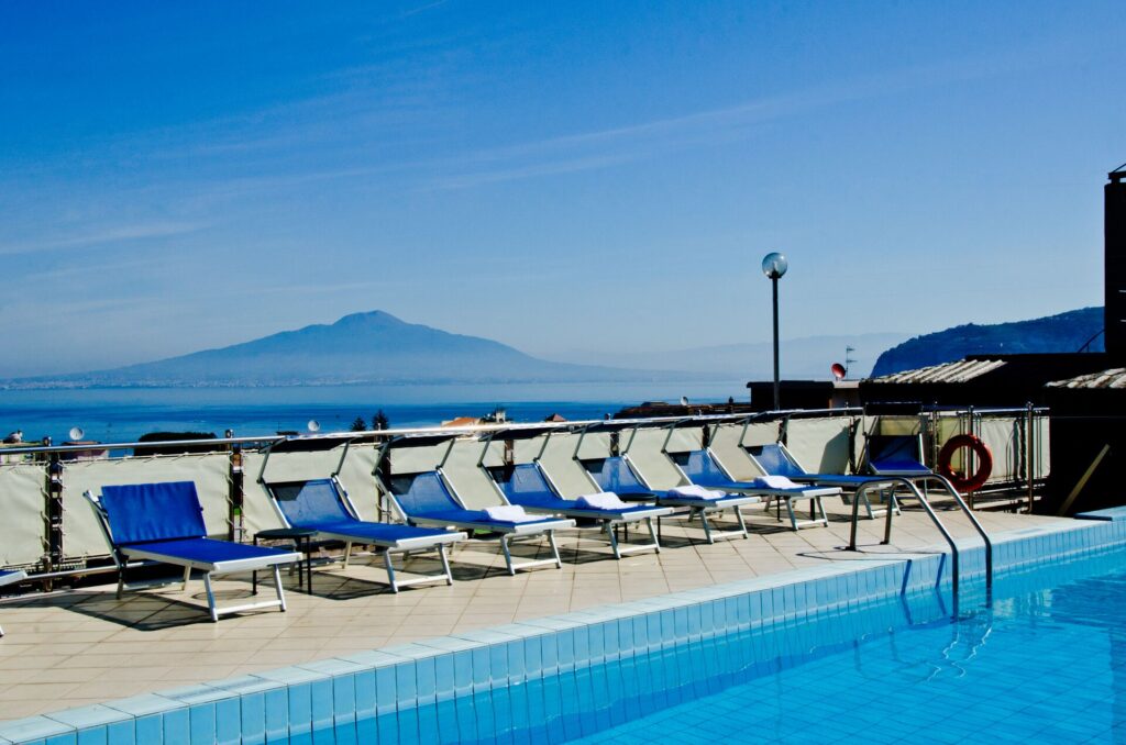 A clear blue swimming pool with deck chairs alongside and a mountain backdrop.