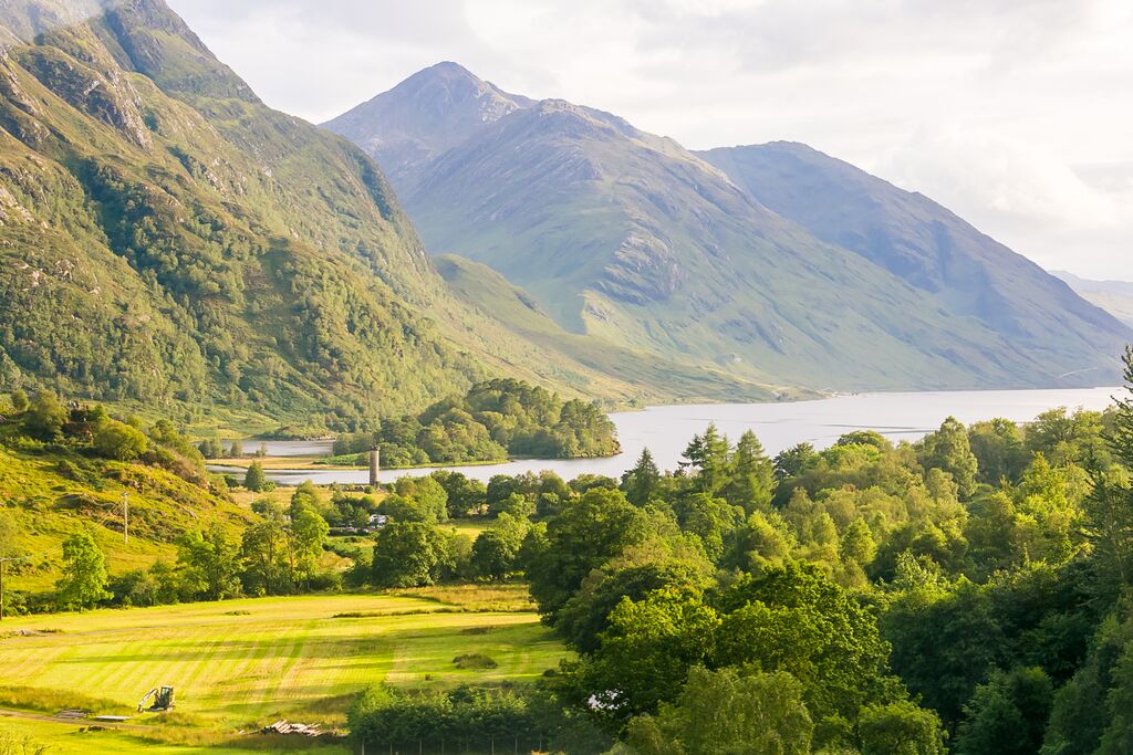 A gorgeous landscape in Scotland: a loch snakes through the countryside with mountains arching in the background, and lush forests sprawling out in the foreground