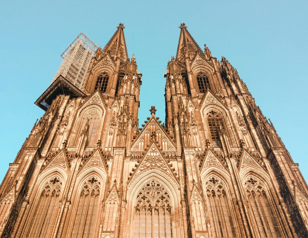 Two ornate spires of Cologne Cathedral rise against a blue sky