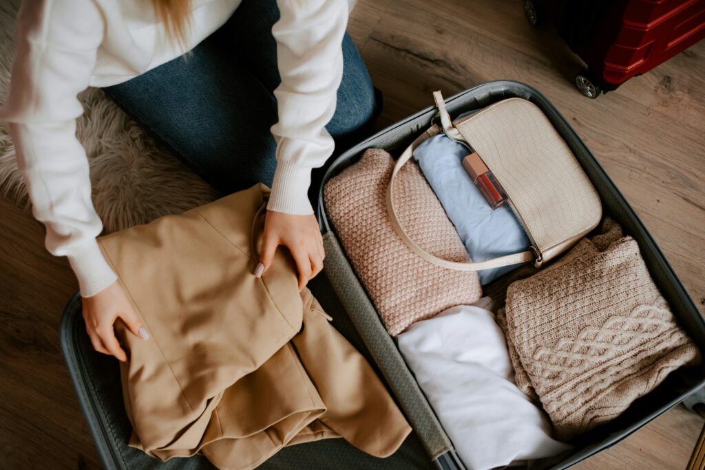 A lady pacing a suitcase, including beige wooled knits and a cream handbag.