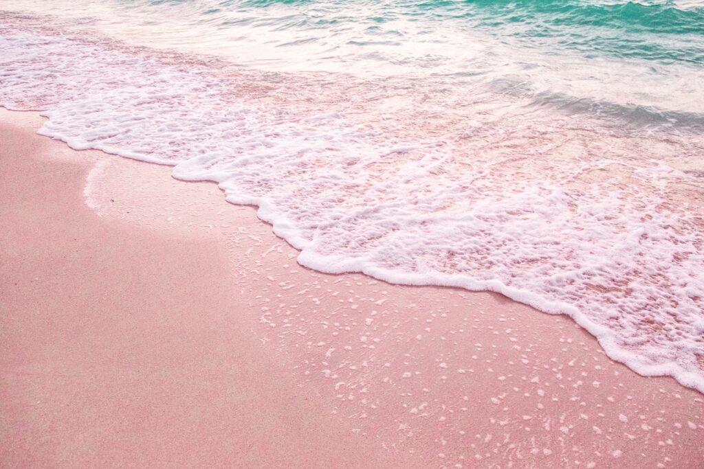 Pale pink sand merges with white foamy waves.