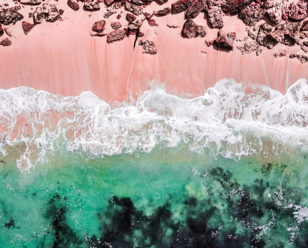 Dark and pink sands are lapped by green waves.