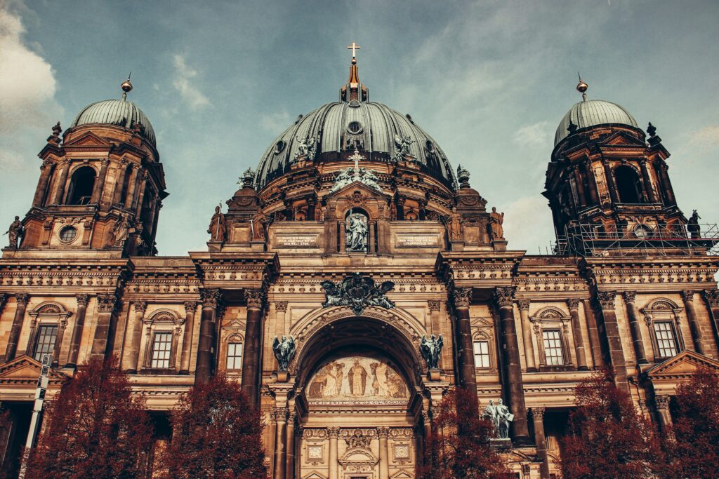 The ornate facade of Berlin Cathedral with green domes and a grey blue sky