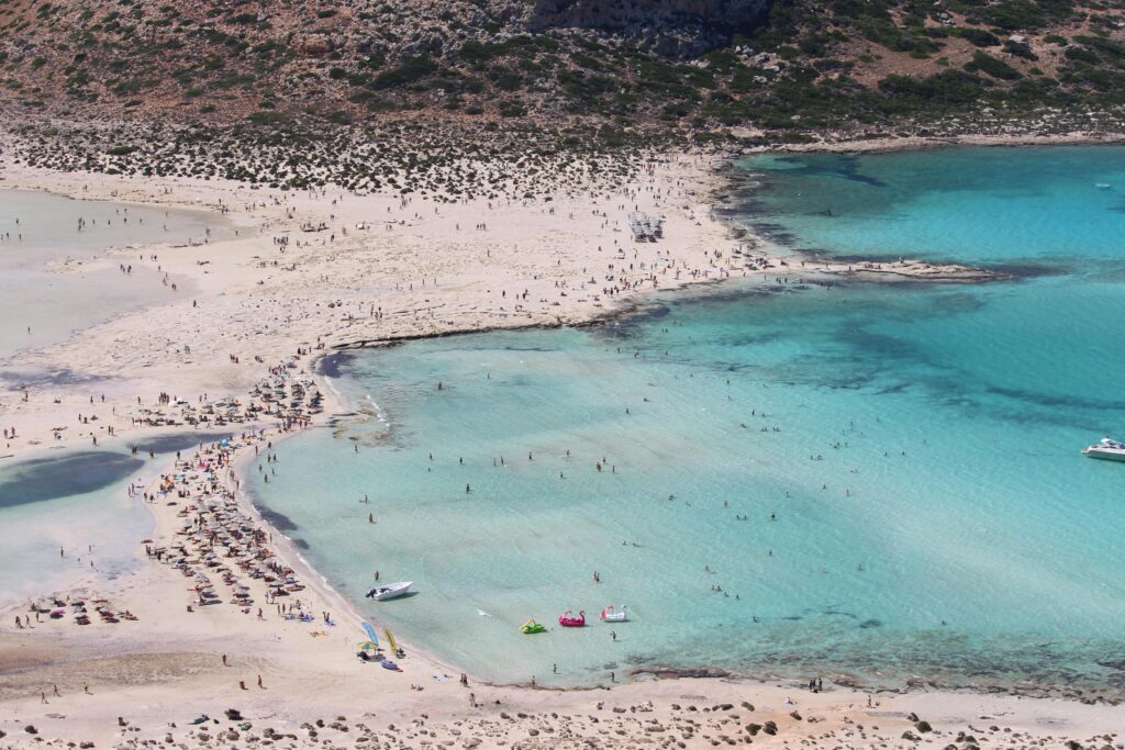 Aerial shot of large pink beach full of people with turquoise water