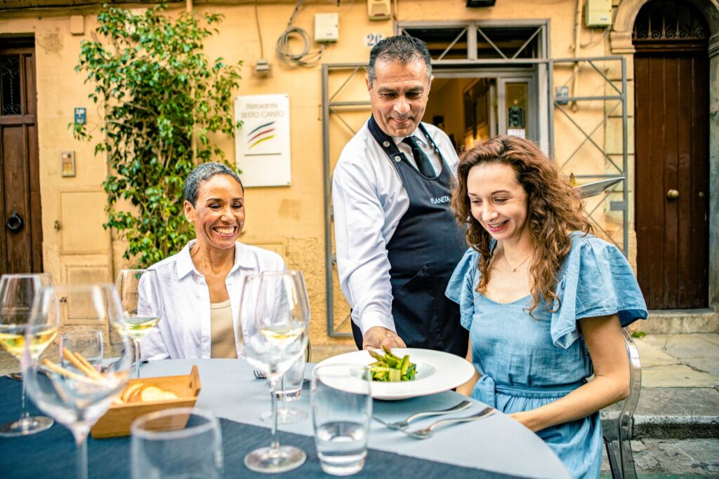Guests dining in palermo, a waiter serves a plate of beautiful Sicilian food