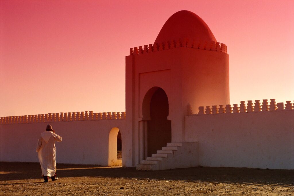 A man walking along a terraced wall in Marrakech, the sky is a rouge sunset