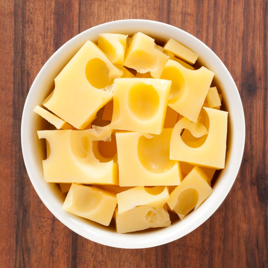 Chinks of Swiss cheese with the distinctive holes in a white pot on a wooden surface.