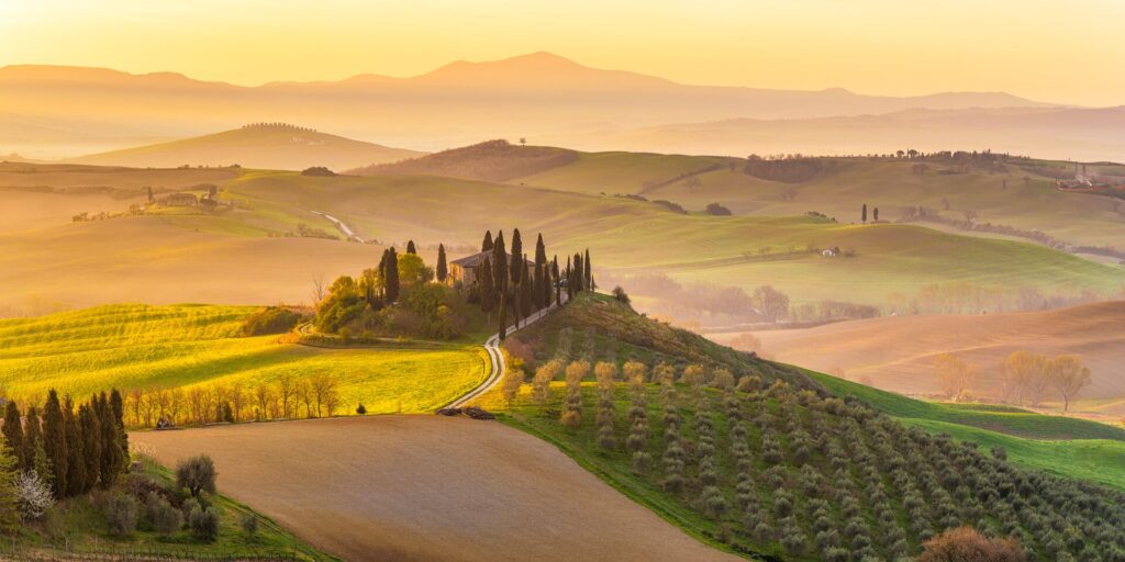 Tuscan countryside in morning sun, misty and hazy with vineyards stretching out into the horizon. one of the best places to visit in october