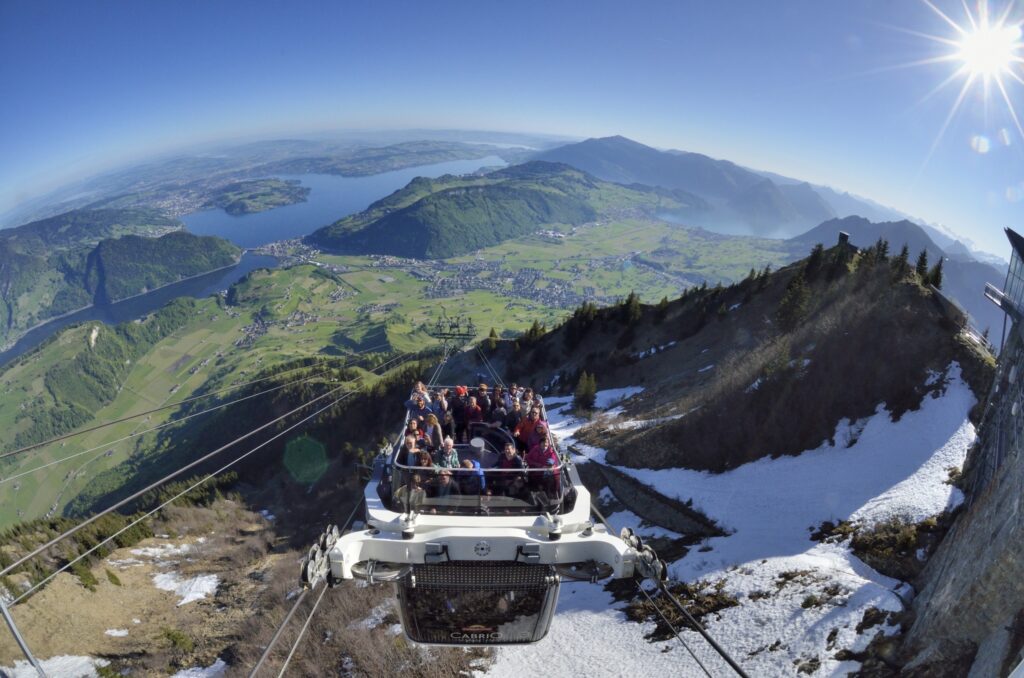 view looking down on a cable car ascending a mountain surrounded by Alpine scenery